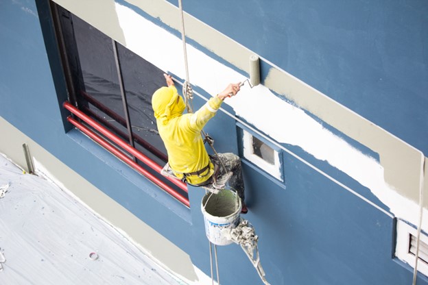 painters hanging on roll, painting color on building wall. facade builder worker with roller brush, working on high building. safety construction with lift rope belt in city.