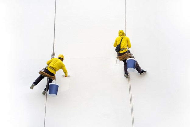 Worker painting wall at high rise building with rope